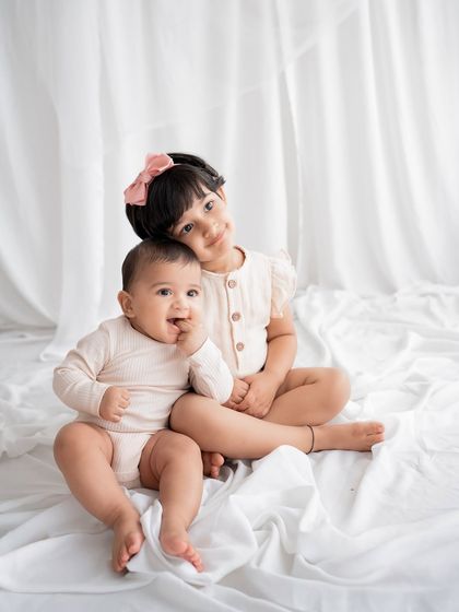 Two sweet siblings sitting together on a white bed.