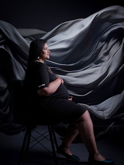An artistic and moody portrait of a mother-to-be. This studio shot uses dramatic lighting and a textured grey backdrop to create a sophisticated and contemplative image.