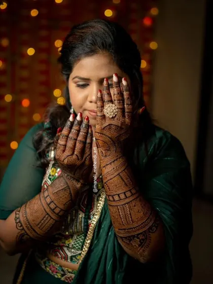 A bride peeking through her hands, which are adorned with a beautifully stained mehandi design. The photo is taken against a festive background, capturing the wedding mood.