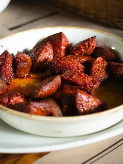 A bowl of spicy Turkish sausage, Suçuk. The light catches the glistening oil, emphasizing its richness and flavor.