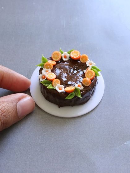 A close-up of a miniature chocolate fruit cake, with tiny orange slices and flowers.