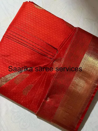 A red saree with a simple gold border, elegantly folded.