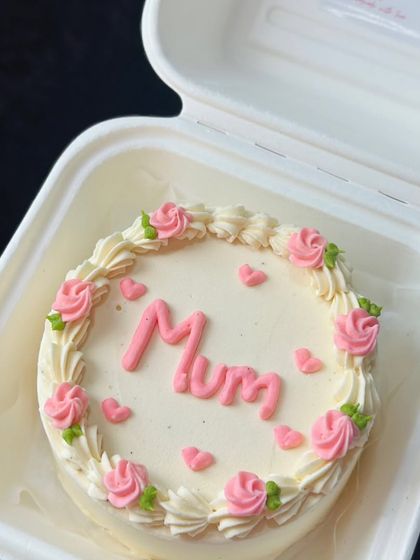 A sweet and simple bento cake for 'Mum'. This design features a border of piped pink roses and tiny hearts, showing that even simple designs are made with love.