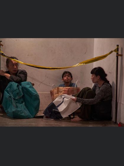 A still from a theatre piece, showing performers huddled together. This image powerfully conveys a sense of displacement and vulnerability, themes I often explore in my collaborative work.