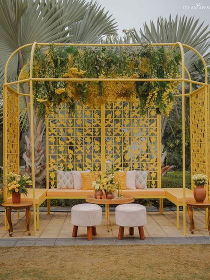 A modern yellow metal cabana with intricate jali work provides a stylish and comfortable seating area.