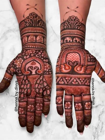 A beautiful symmetrical design featuring peacocks and swans under ornate arches. The wrists are adorned with a band of elephants, adding to the traditional charm.