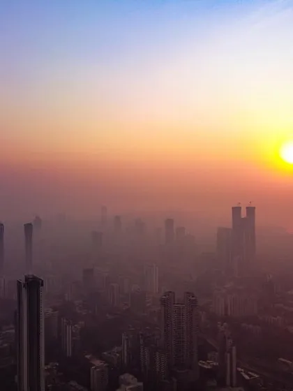 A high-altitude drone shot of the sun setting over a smog-filled Mumbai, creating a scene reminiscent of Delhi's hazy winters.