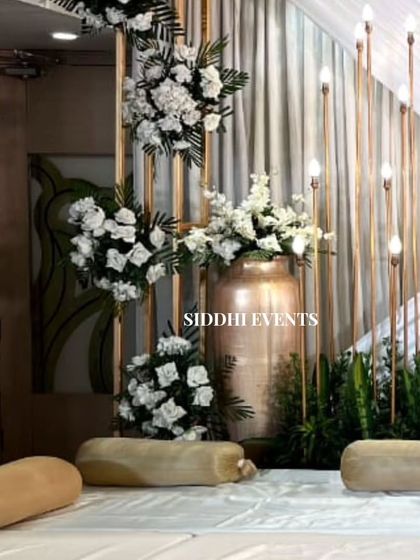 A serene and elegant setup with low floor seating, accented by tall, glowing candle-like lights and arrangements of pure white flowers.