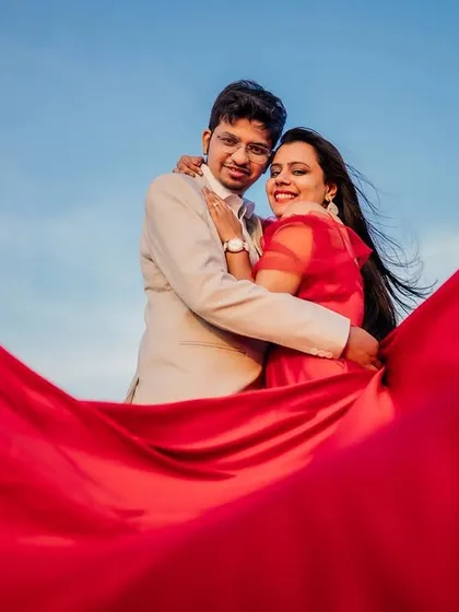 Using the bride's dramatic red dress to frame the couple against a bright blue sky, creating a vibrant and dynamic pre-wedding portrait.