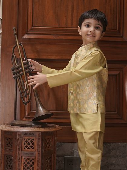 Another angle of our golden-beige Bundi set, showing the young model holding a trumpet. It’s an outfit made for celebration and joy.