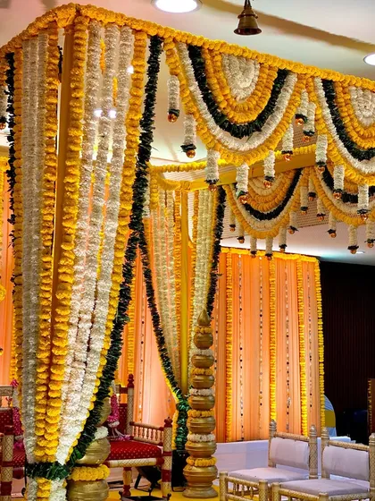 A classic vidhi mandap for a wedding ceremony, built with pillars of yellow marigolds and a canopy of white and yellow flower garlands. This is a traditional and sacred space for wedding rituals.