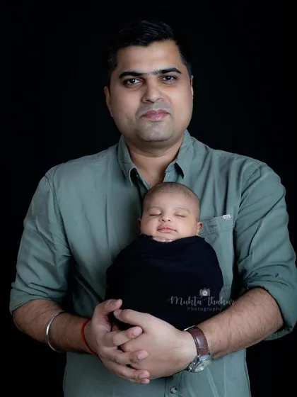 A proud father holds his sleeping newborn, a simple and powerful portrait that highlights the bond between them.