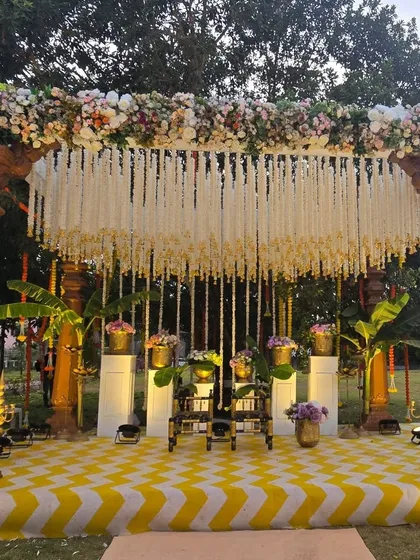 A beautiful South Indian themed Haldi ceremony set in a lush green lawn. The decor features a traditional mandap with heavy floral work, hanging jasmine garlands, and classic banana leaf accents for an authentic and elegant feel.