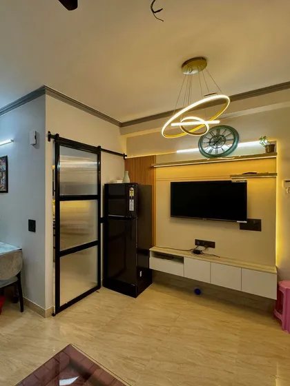 A compact TV cabinet design in a white and light wood finish, with a shelf for decor and a modern ring-shaped chandelier.