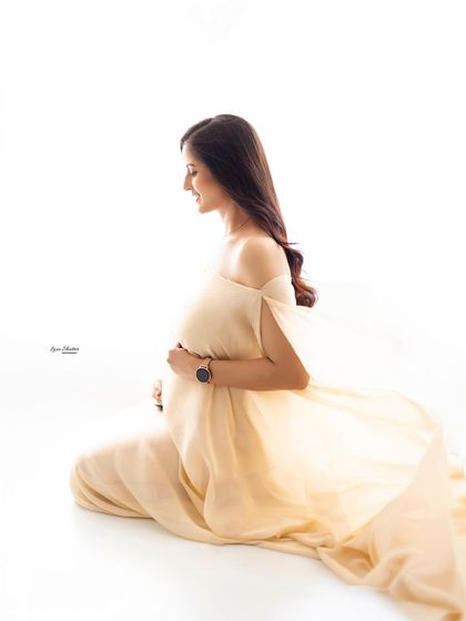 A quiet, contemplative profile shot. The soft, flowing fabric of the gown and the simple white background create a peaceful and elegant image, focusing on the beautiful silhouette.