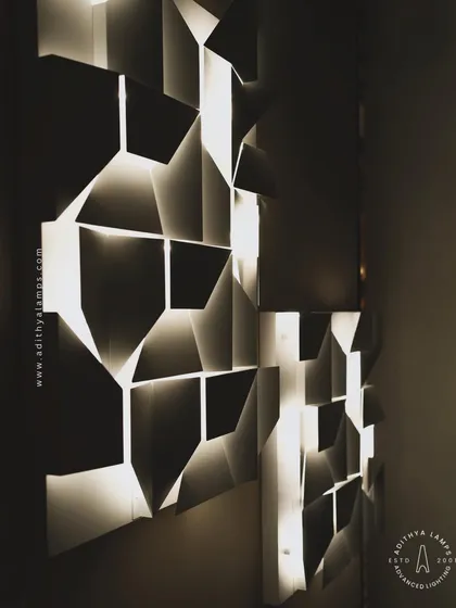 Another dramatic, low-light shot of the geometric wall light. This angle emphasizes the contrast between the illuminated edges and the shadowed faces of the panels, creating a highly textural and visually engaging effect.