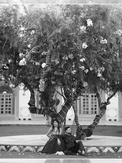 A serene black and white portrait of the couple sitting together under a large, beautiful tree. This quiet, candid moment feels peaceful and deeply connected.
