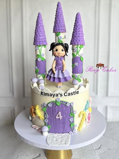 Welcome to Kimaya's Castle. This enchanting cake is designed like a purple fairytale castle, complete with towers, a wooden door, and a princess figure, perfect for a 4th birthday.