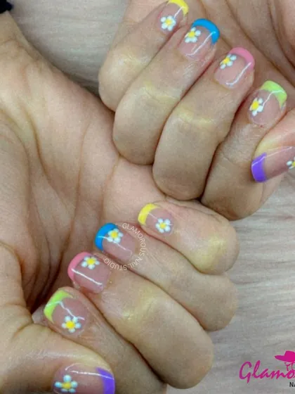 A fresh and fun take on the French manicure, this design features multi-colored pastel tips and is adorned with small, hand-painted white daisies.