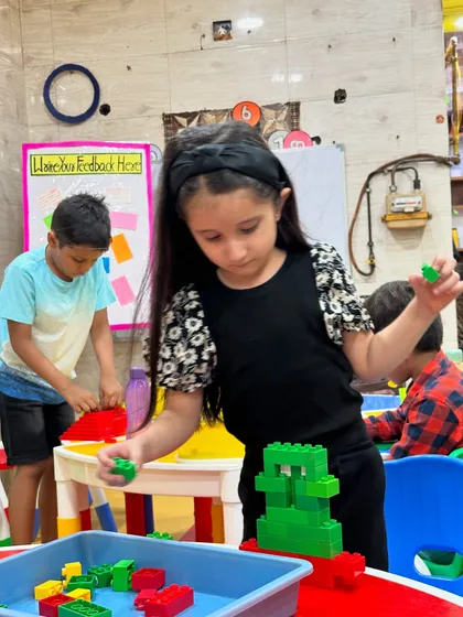 A girl concentrates on her LEGO creation, carefully placing green blocks onto her structure.