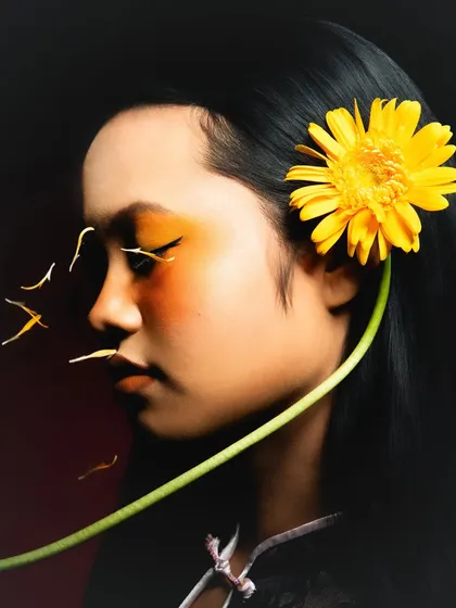 This shot captures the feeling of sunlight and nature. The earthy, yellow-orange tones on the eyes and cheeks are paired with sleek hair and a single flower for a botanical beauty statement.