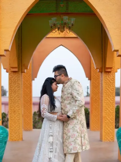 A tender moment captured during a pre-wedding shoot. The groom-to-be kisses his partner's forehead, both dressed in elegant, coordinated ethnic wear.