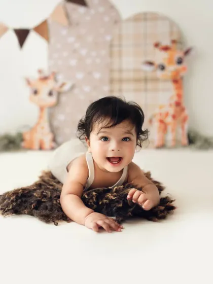 A baby lies on a fluffy rug, smiling brightly during his half-birthday photoshoot. These tummy-time shots are great for capturing this stage.