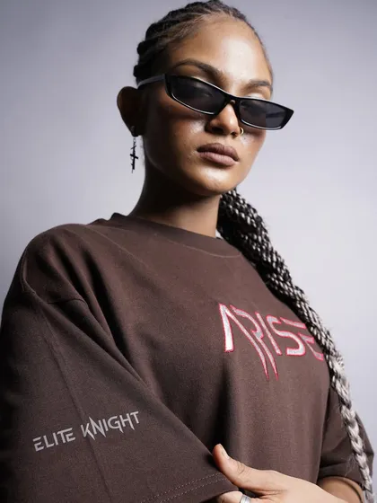 A close-up portrait of the model wearing the 'ARISE' tee, showing off her cool sunglasses and braids. This shot is all about attitude and personal style.