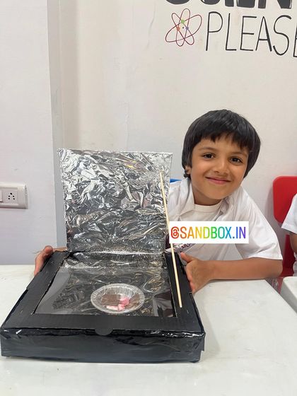 He's all smiles with his finished solar cooker project. Building this taught him how angled reflectors can concentrate sunlight to generate more heat.