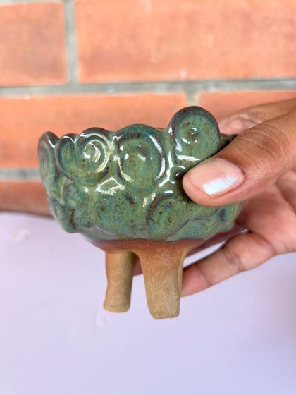 A small, three-legged bowl with a beautiful textured green glaze, made by a student named Poonam during her 15-day course.