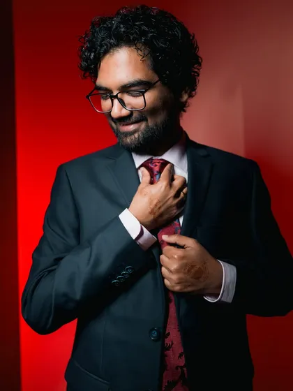 A candid-style portrait of the groom adjusting his tie against a vibrant red background.