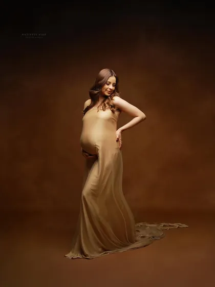 A graceful pose in a sheer golden gown against a painterly brown backdrop. This studio shot focuses on the beautiful curves of pregnancy.