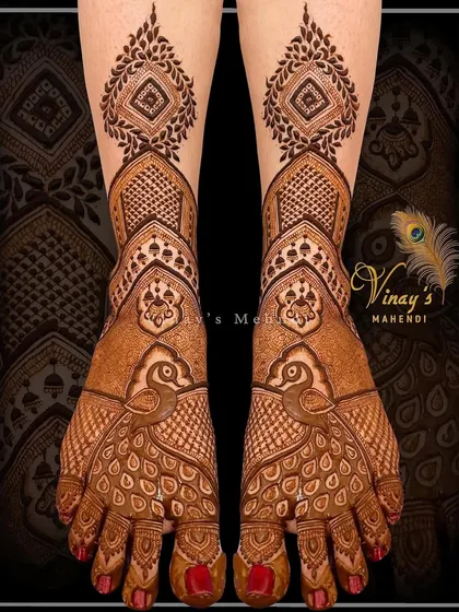 A modern take on foot mehndi, with peacock motifs on the feet and a geometric pattern extending up the leg.