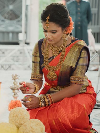 A bride lighting a lamp during a ceremony. Her orange saree glows in the warm light, creating a beautiful and auspicious image.