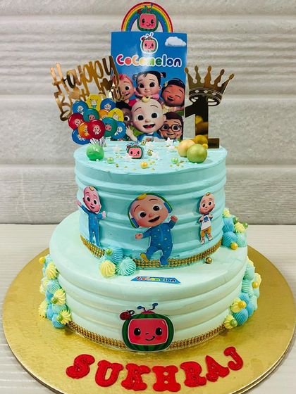 A grand two-tiered Cocomelon cake for a first birthday celebration. It's covered in characters from the show and decorated with colorful details.