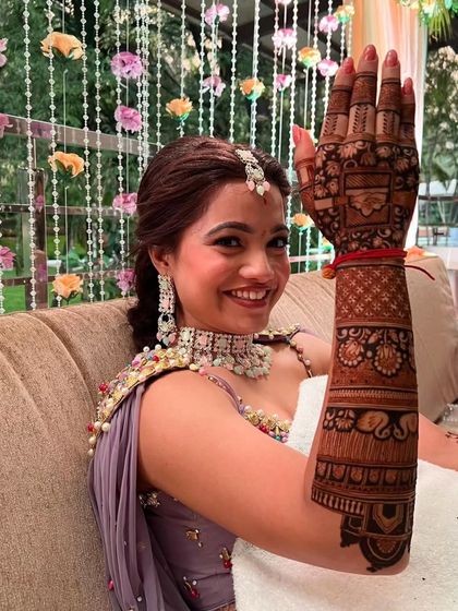 A happy bride showing her palm, which is covered in a beautiful and intricate mehandi design.
