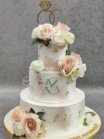 A beautiful three-tiered vintage wedding cake for a special couple. The soft pink marble effect, delicate gold leaf flakes, and fresh roses create a romantic and timeless look. The custom monogram adds a personal touch to this engagement cake.