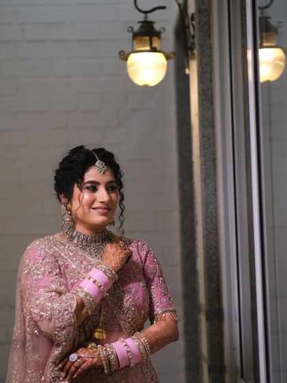 A bride's quiet moment of reflection before the ceremony. The soft light and her elegant pink lehenga create a portrait of grace and anticipation.