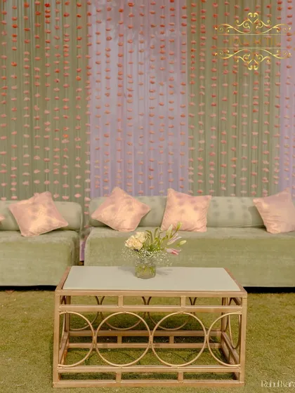 A comfortable lounge area with pastel green sofas, set against a backdrop of hanging sola flower strings.