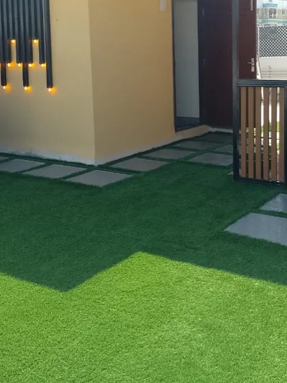 This angle showcases the layout of the terrace, with stone pavers creating a pathway across the artificial turf. The wall-mounted lights add a modern touch and provide ambient lighting.