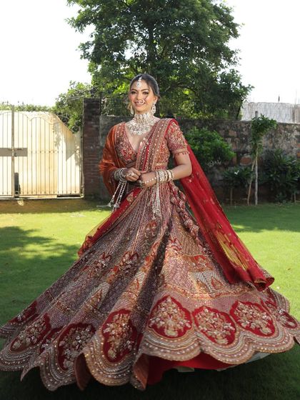 A full-length shot of a bride looking radiant in our intricately embroidered red and orange lehenga. The perfect outfit for a grand outdoor wedding.
