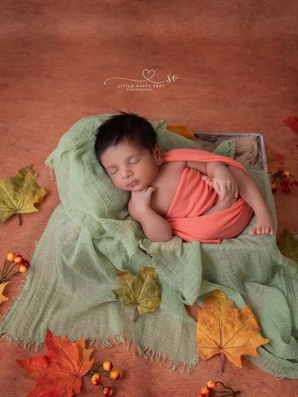 An autumn-themed flat-lay. The simple arrangement of colorful leaves around the sleeping baby creates a beautiful and artistic seasonal portrait.
