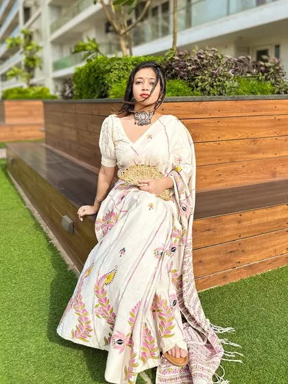 A full-length seated pose, showing the intricate kantha stitch work on the pallu of the saree.