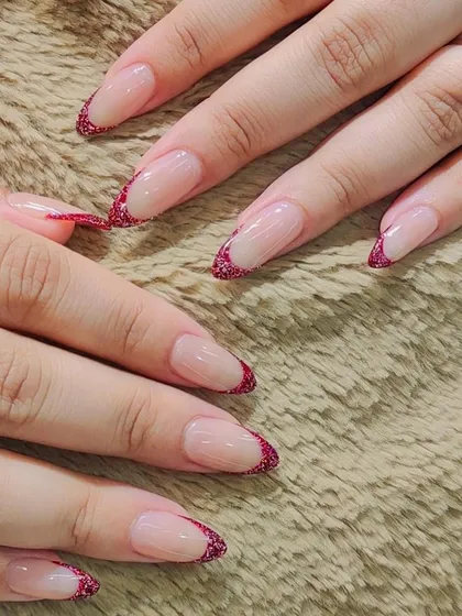 A chic and modern French manicure. The tips are filled with a sparkling red glitter, offering a festive and glamorous twist on the timeless style.