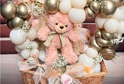 A cuddly teddy bear takes center stage in this beautiful welcome basket. Surrounded by a heart-shaped balloon frame in gold and white, and accented with baby's breath, it's a warm and inviting gift for a newborn.