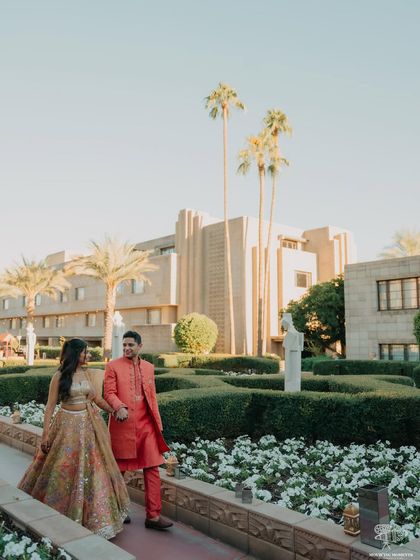 A wide shot of the couple walking through the manicured gardens of the Arizona Biltmore. The grand architecture and beautiful landscape provide a stunning backdrop for their portrait.