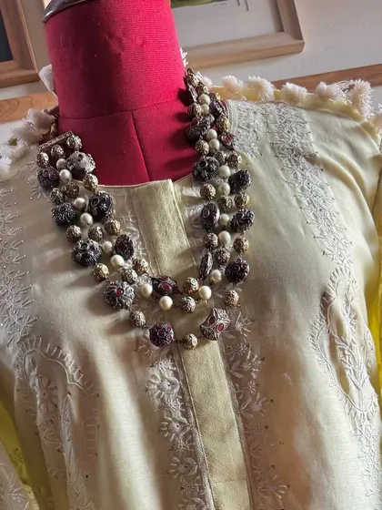 A close-up of the neckline of our lemon yellow kurta, styled with a statement necklace. The image highlights the fine Chikankari and the playful tassels lining the sleeves and hem.