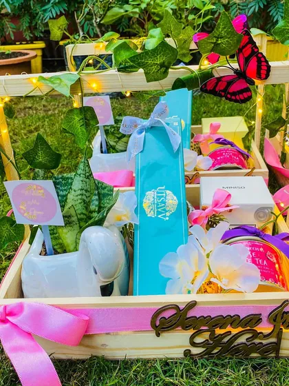 I designed this whimsical baby announcement hamper in a personalized wooden crate featuring the baby's name in a beautiful cutout. The 'Butterfly Garden' theme is brought to life with fairy lights, lush greenery, and carefully selected gifts like a swan-shaped planter and rose-flavored white tea.