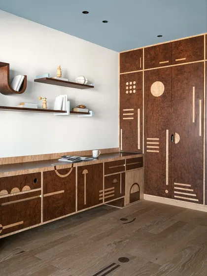 Storage should never be boring. For this multipurpose room, we designed a full-wall unit in rich burl veneer with intricate geometric inlays. The design combines different shutter types and playful motifs, with a surprise pop of mint green inside, turning a practical piece into a visual delight.