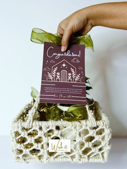 A beautiful housewarming gift basket, featuring a macrame-style holder, a small plant, and a custom "Congratulations" card.